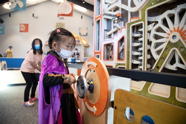 A child spins a lever to move parts of the ball machine