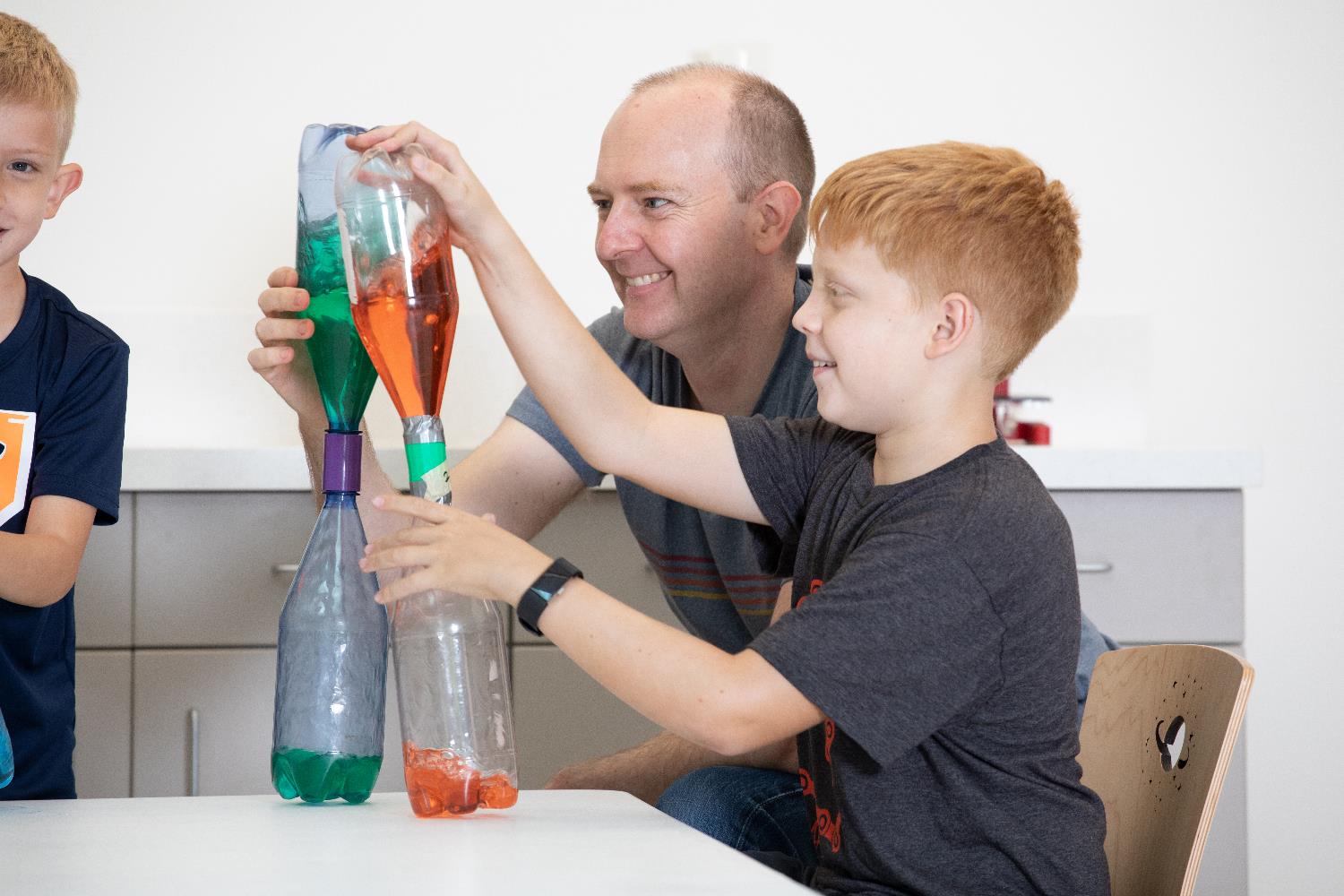 An instructor sits next to a child as they compare their science experiments