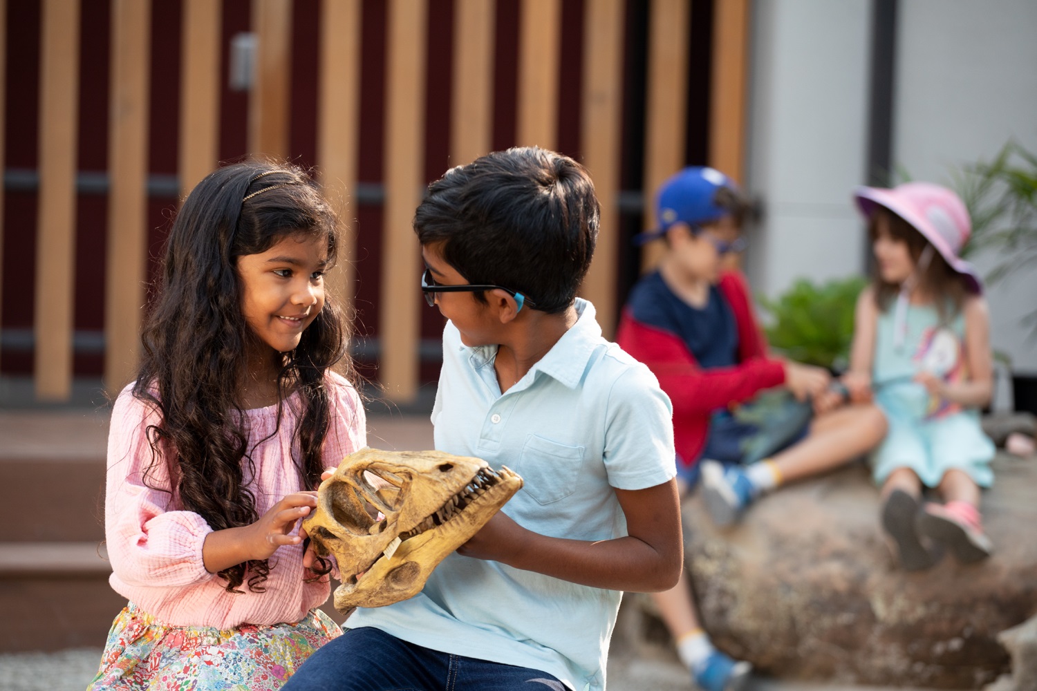 Two kids look at each other while holding a dinosaur fossil