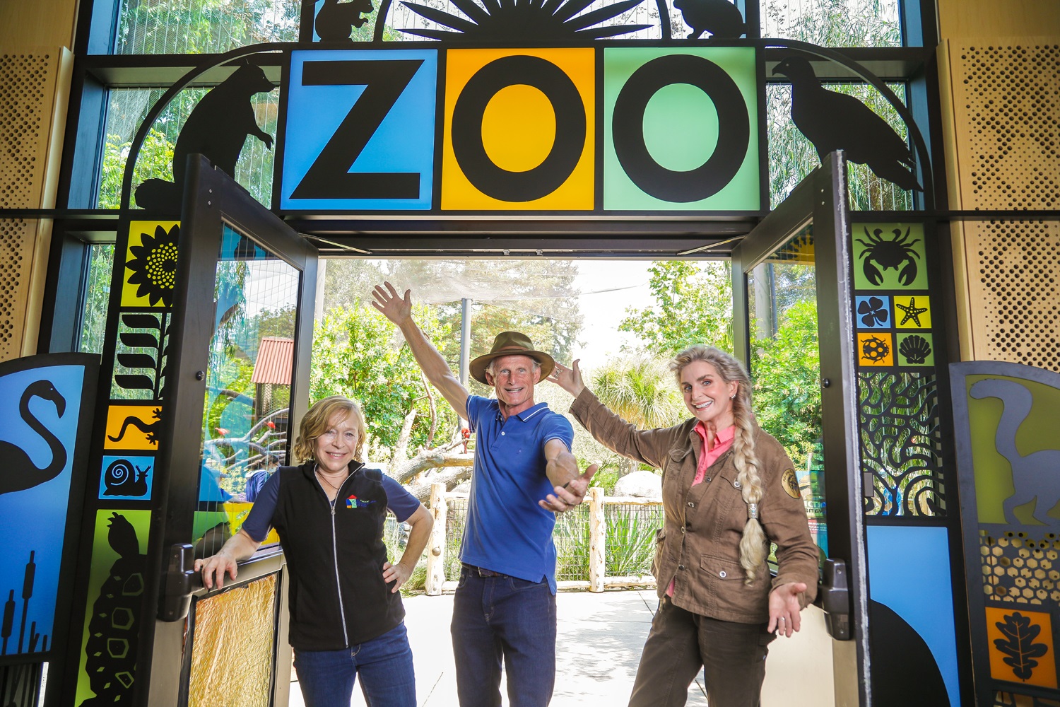 Alex, John, and Lee stand in front of the doors to the zoo, holding them open in a welcoming gesture.